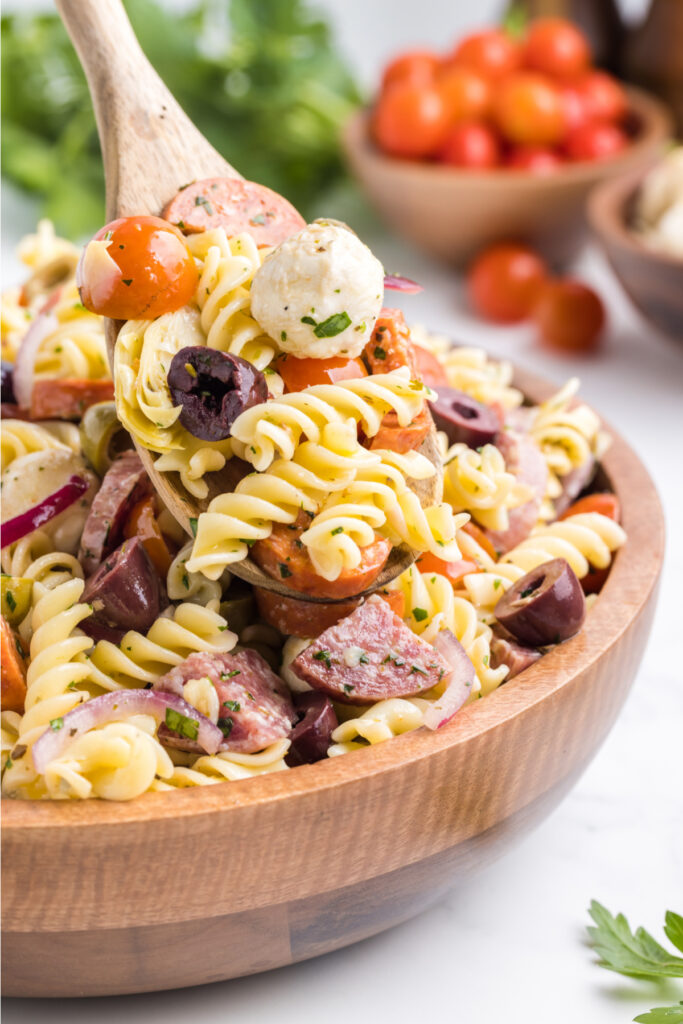 wooden spoon scooping antipasto pasta salad out of a wooden serving bowl